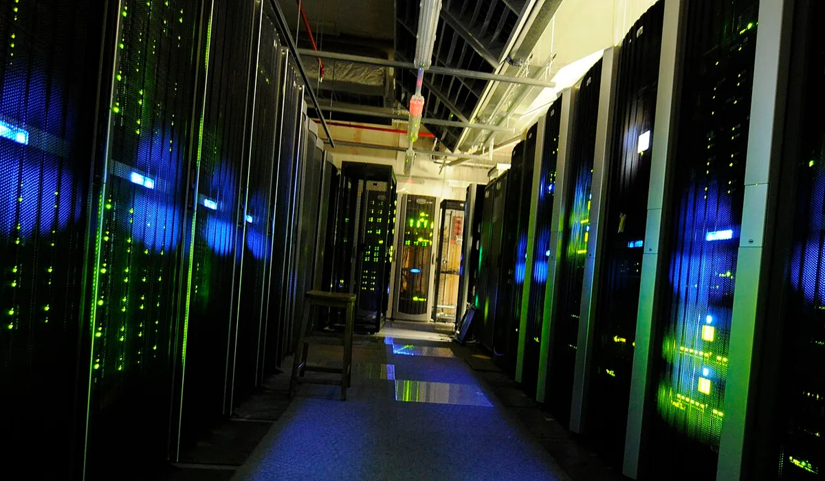 Gang tussen twee rijen serverkasten in een datacentrum, met blauwe en groene statuslampjes die weerspiegelen in de vloer.