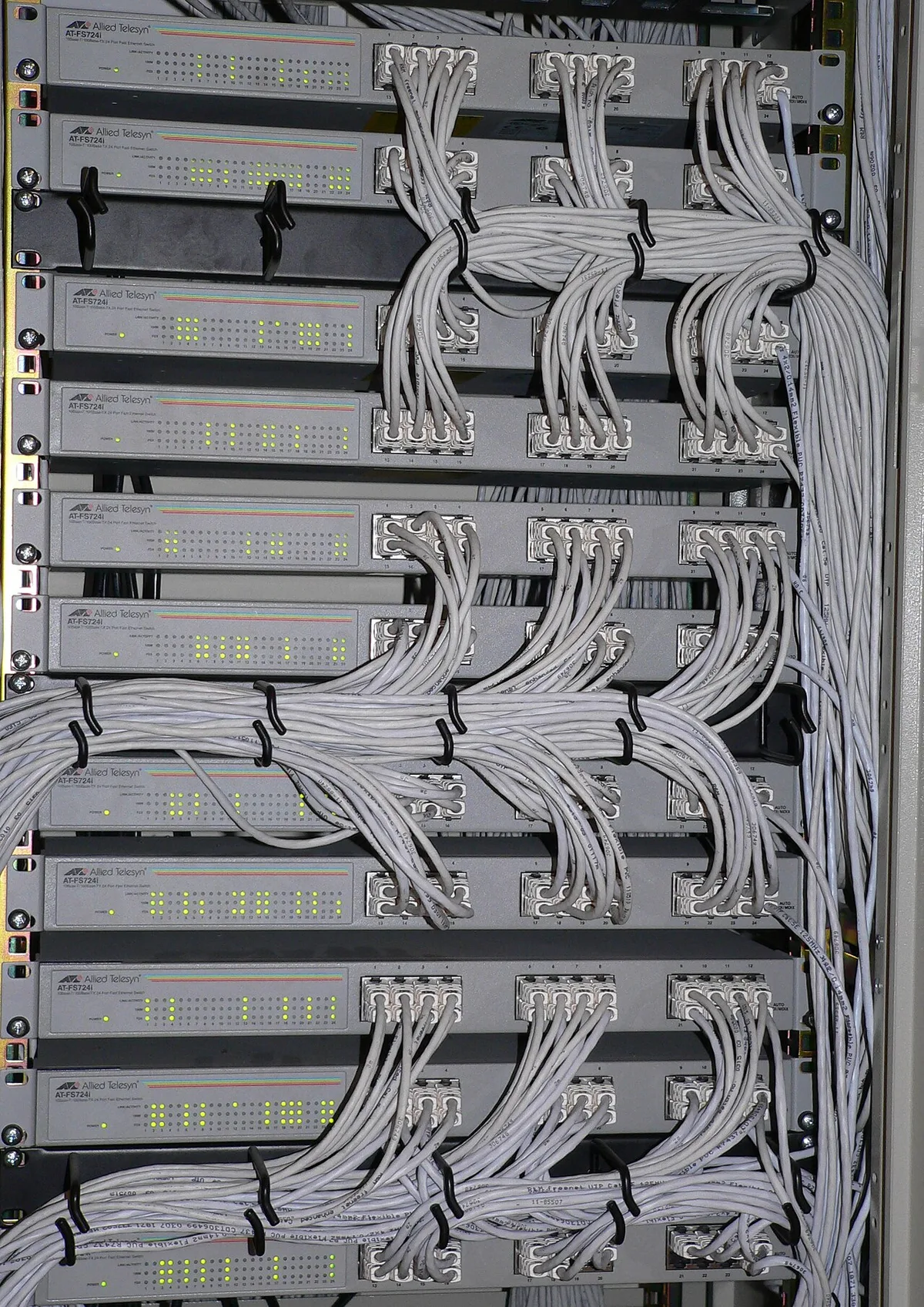 Netwerkswitches in een serverkast met keurig gebundelde grijze patchkabels die in bogen naar de aansluitpanelen lopen.